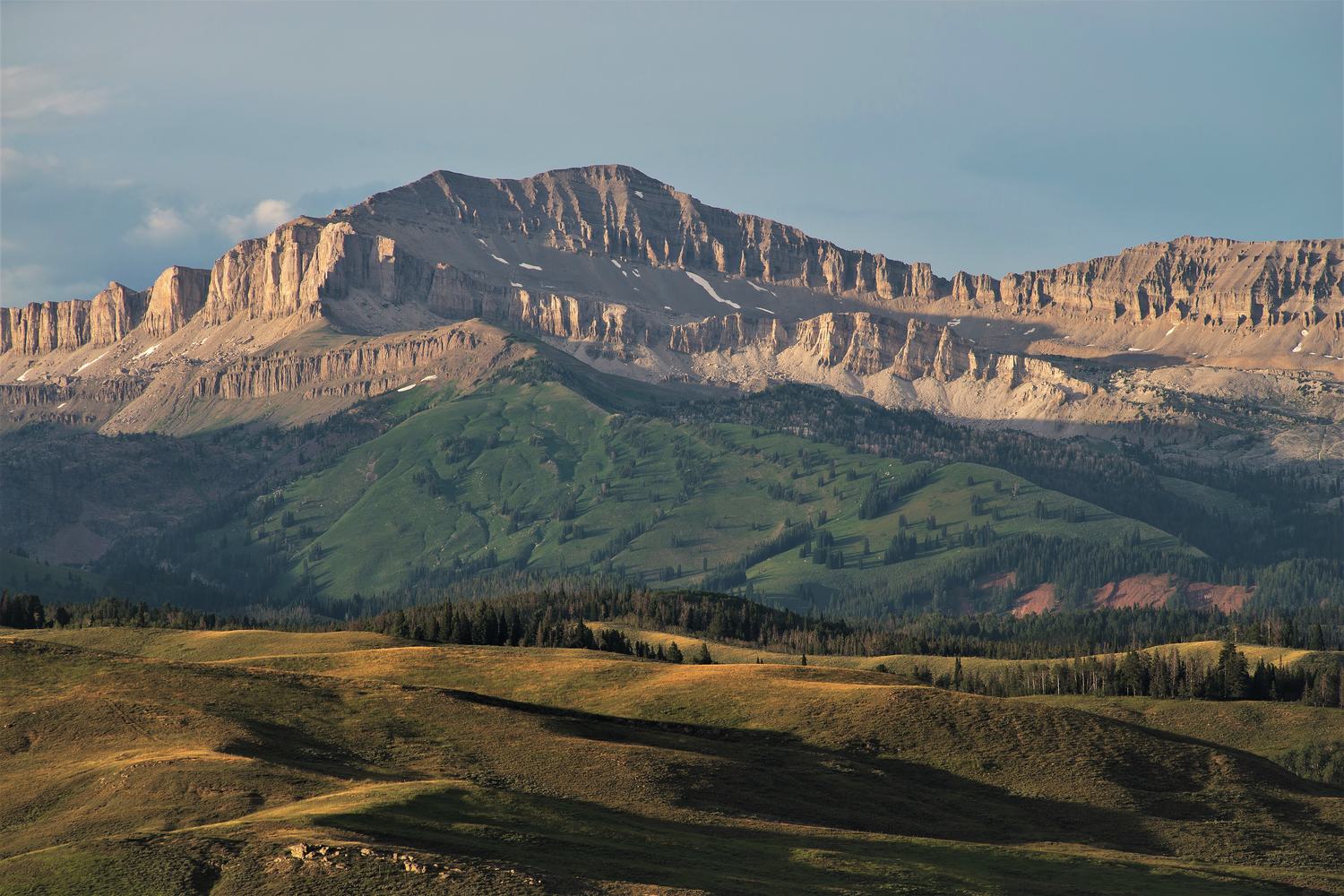 The layered south face of Doubletop Peak in the Gros Ventre Range above rolling meadow and timber.