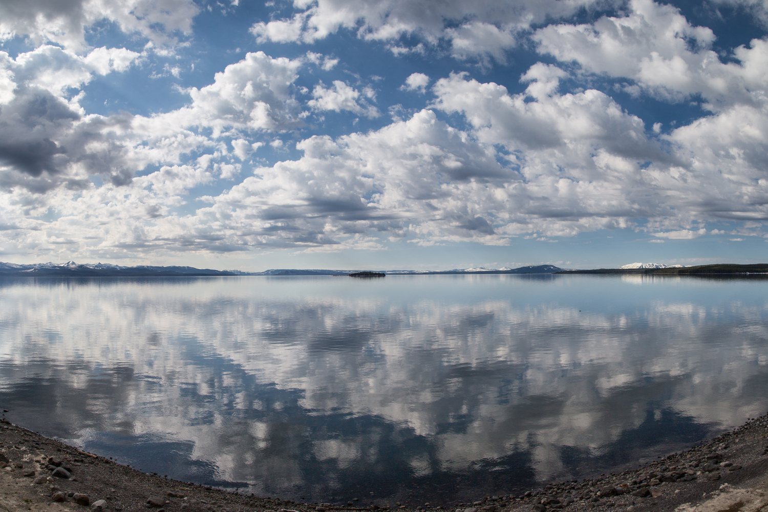 Banks of cloud mirrored in the flat water of Yellowstone Lake with low hills on the far shore.